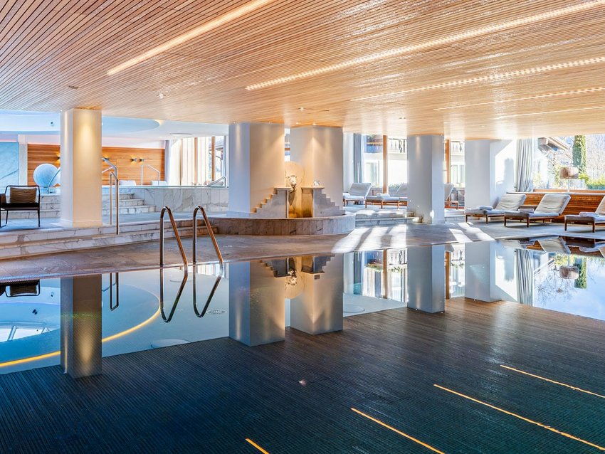 Your spa hotel in Allgäu: Allgäu Sonne Indoor pool area with wooden ceiling, lounge chairs, and large windows with mountain view