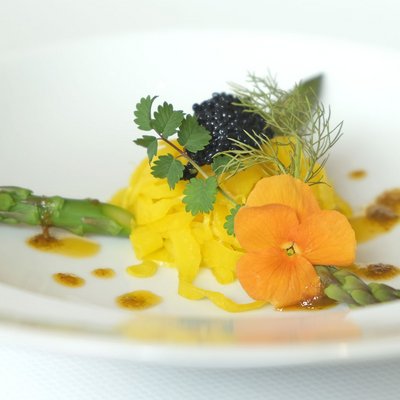 Feine Gourmetplatte mit grünem Spargel, essbarer Blume und Kaviar auf weißem Teller