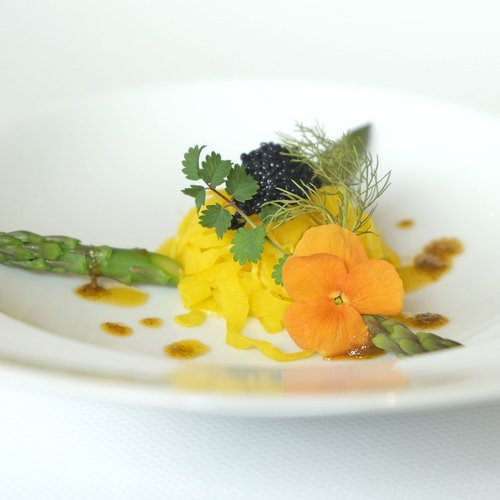 Feine Gourmetplatte mit grünem Spargel, essbarer Blume und Kaviar auf weißem Teller