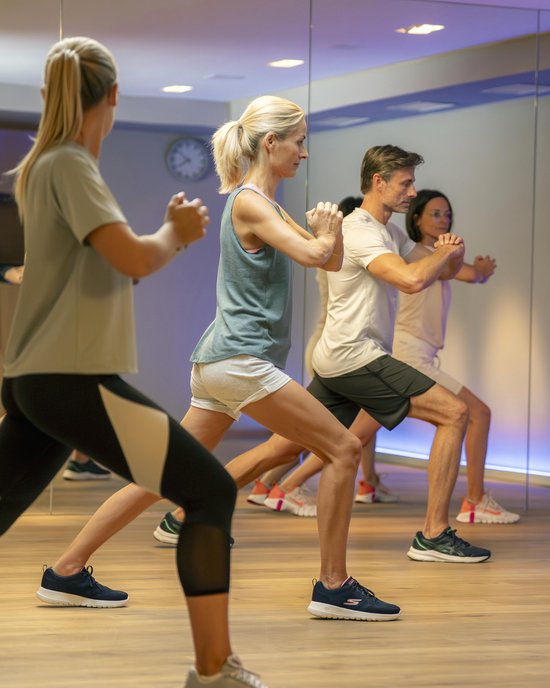 Fitnessgruppe macht Dehn- und Gleichgewichtsübungen im Studio vor Spiegel