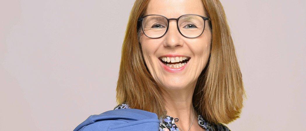Lächelnde Frau mit Brille, Blumenbluse und blauem Pullover über der Schulter