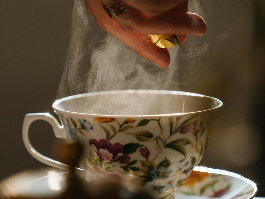 Hand gibt Blume in dampfende Teetasse mit floralem Muster