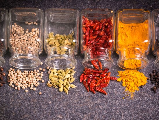 Various spices including cloves, white peppercorns, cardamom, dried chili, and turmeric on dark surface
