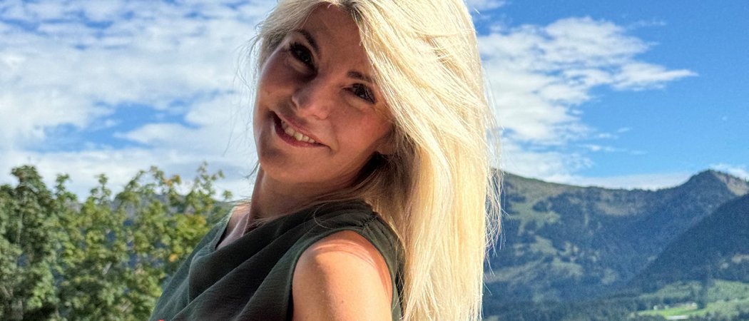 Wissen, das inspiriert: Unsere Vortragsreihe greift Themen auf, die das Leben bereichern. Blonde Frau mit Buch vor Berglandschaft und blauem Himmel