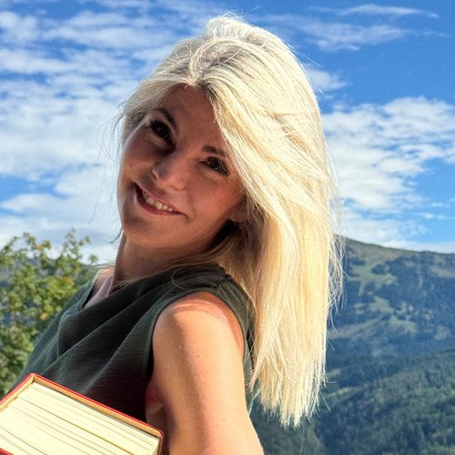 Wissen, das inspiriert: Unsere Vortragsreihe greift Themen auf, die das Leben bereichern. Blonde Frau mit Buch vor Berglandschaft und blauem Himmel