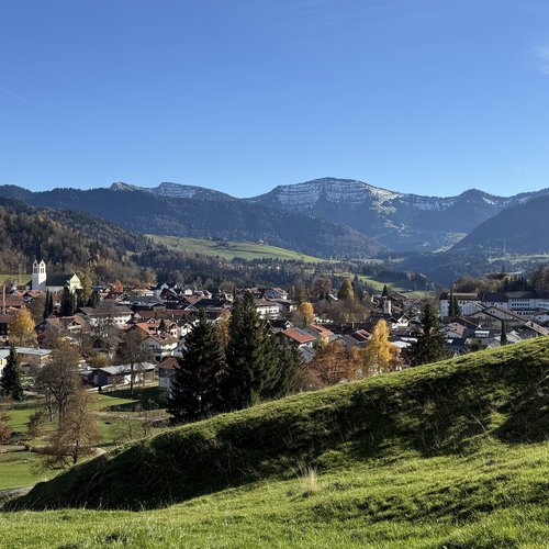 Blick auf ein Dorf mit Kirche und schneebedeckten Bergen unter klarem Himmel