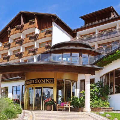 Ihr 5-Sterne-Hotel im Allgäu - Luxusurlaub in den Bergen Eingang eines Hotels im alpinen Stil mit Holzbalkonen und Blumen