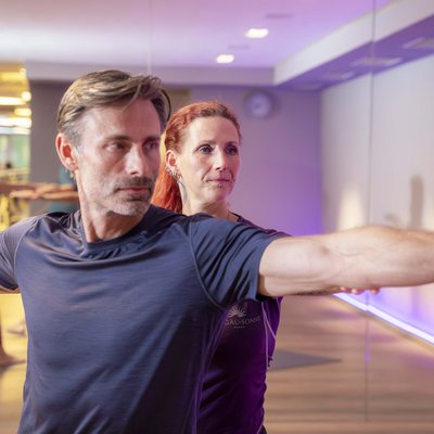 Yoga-Lehrer hilft Mann bei Dehnübung in hellem Fitnessstudio