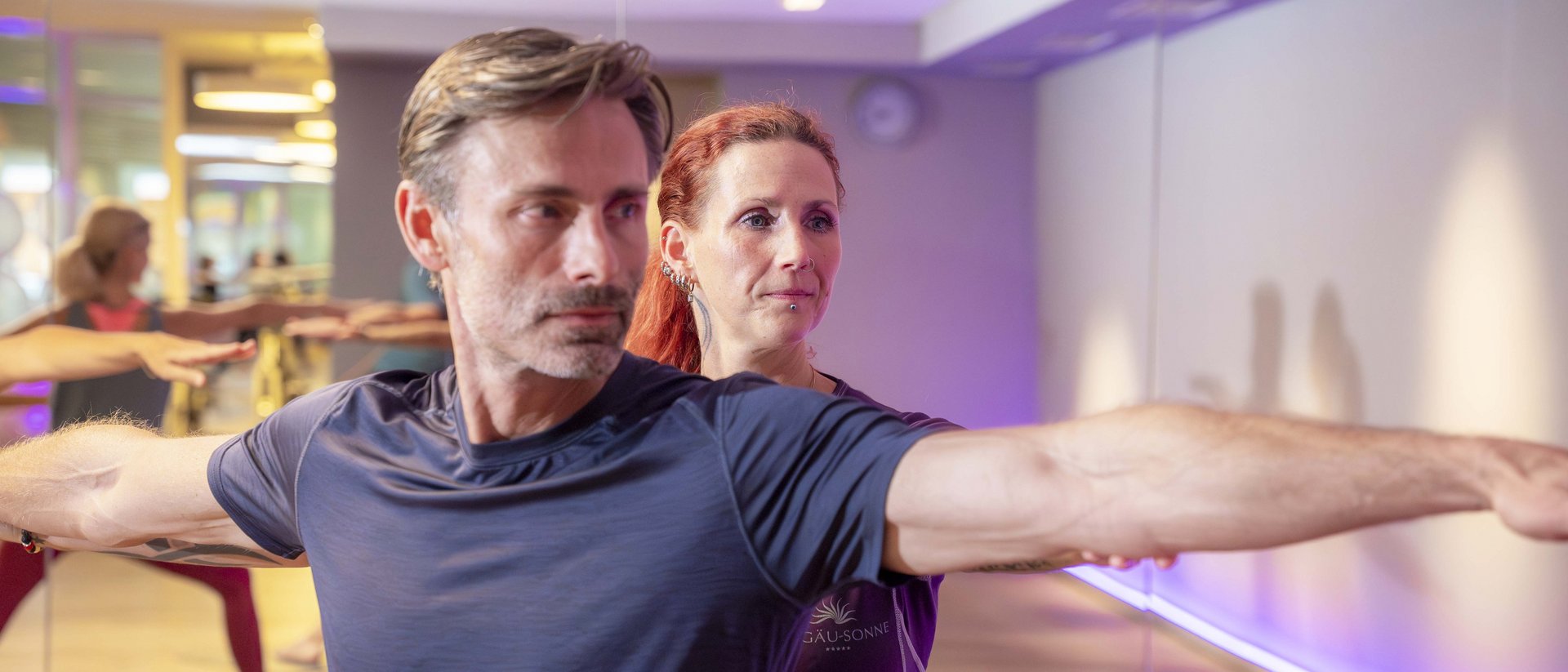 Yoga-Lehrer hilft Mann bei Dehnübung in hellem Fitnessstudio