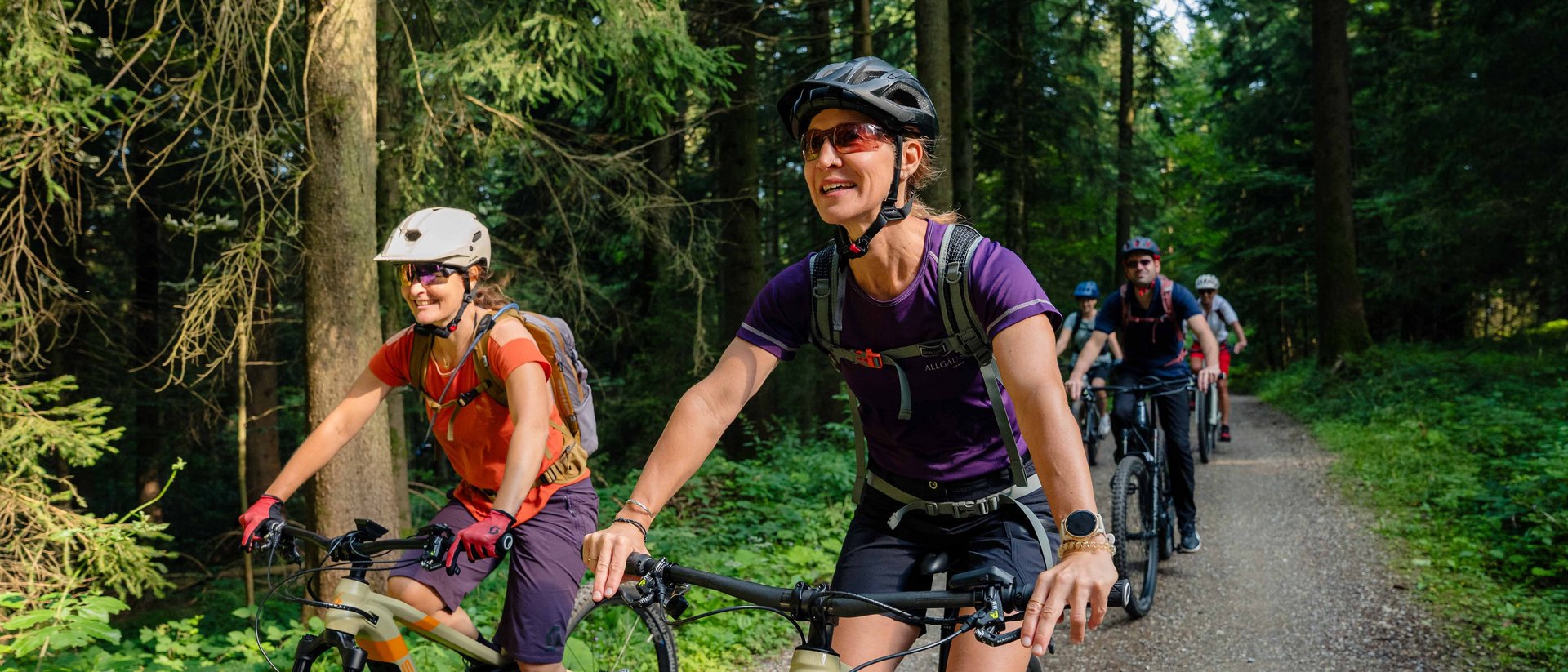 Gruppe von Menschen beim Mountainbiken auf einem Waldweg an einem sonnigen Tag