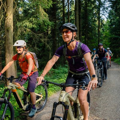 Gruppe von Menschen beim Mountainbiken auf einem Waldweg an einem sonnigen Tag