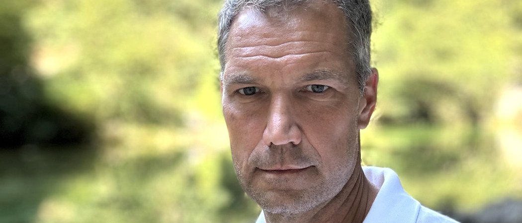 Nahaufnahme eines ernst blickenden Mannes vor unscharf grünem Hintergrund