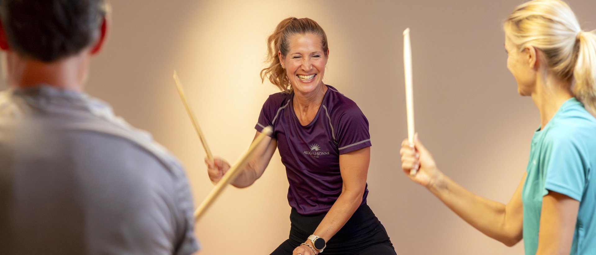 Three people happily playing fitness drums with sticks indoors
