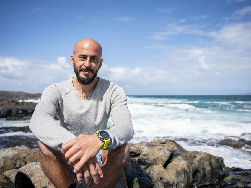 Das Breathwork Retreat Mann mit Bart und grauem Pullover sitzt auf Felsen am Meer bei sonnigem Wetter