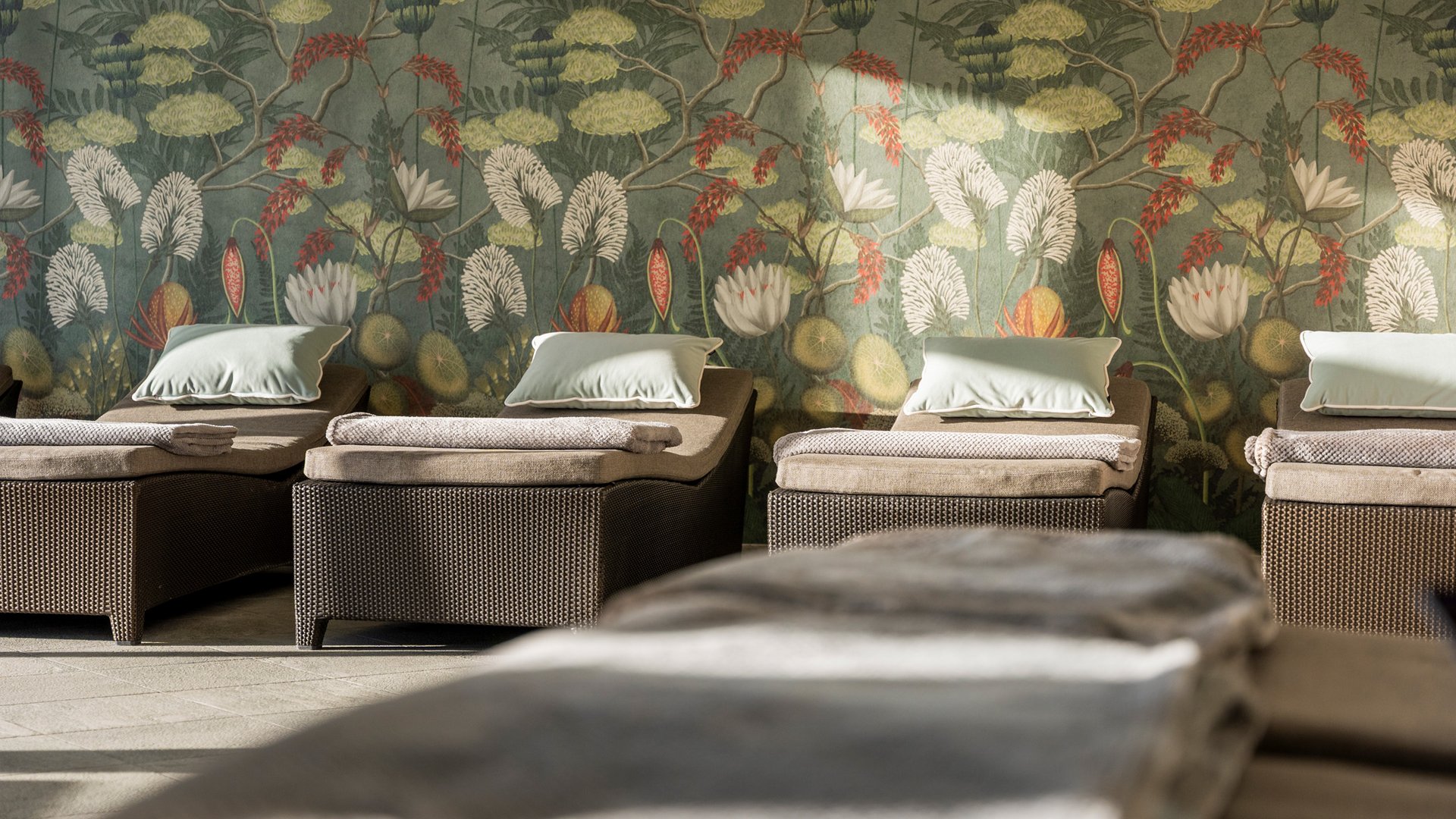 Entspannte Liegestühle mit Kissen vor einer Wand mit floralem Muster