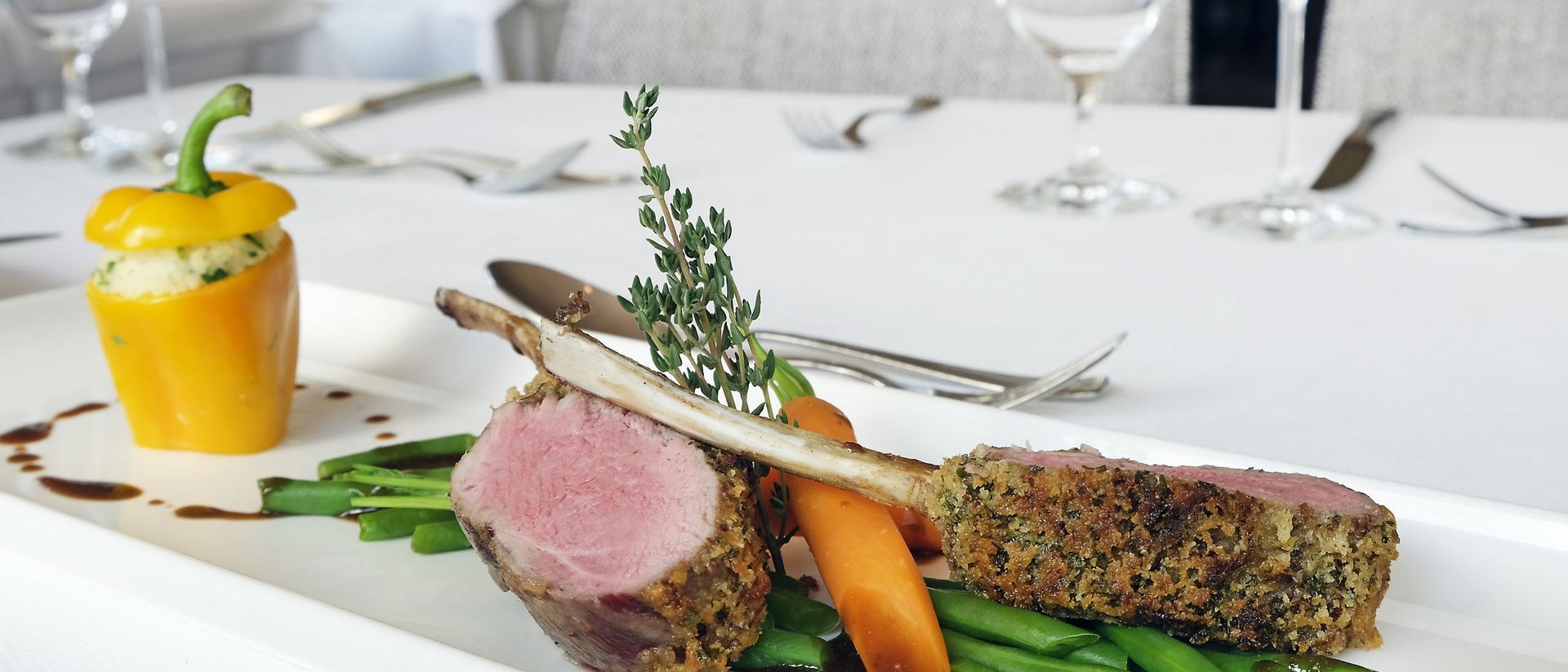 Gedeckter Teller mit Lammkoteletts, grünen Bohnen, Karotte und gefüllter gelber Paprika