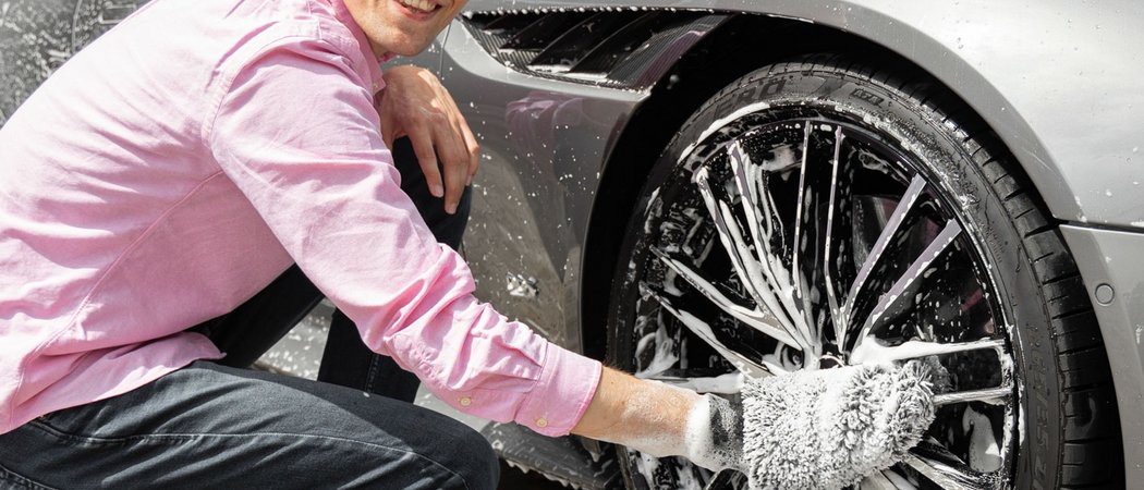 Wissen mit Weitblick – Vortragsreihe im Allgäu | Hotel Allgäu Sonne Mann wäscht Autoreifen mit Schwamm und Schaum neben silbernem Sportwagen