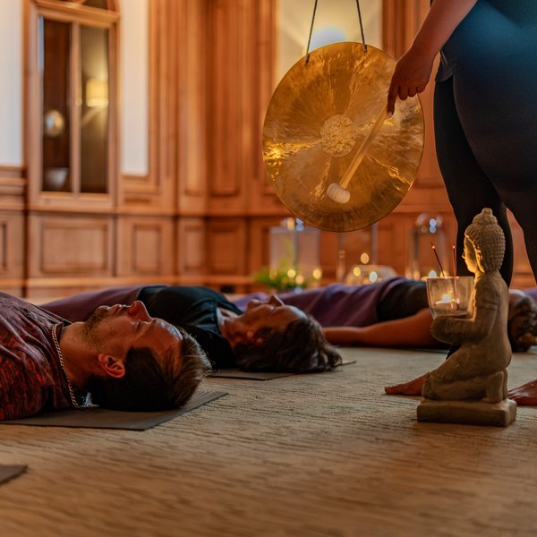 NEU: Yoga- & Ayurveda-Retreat Personen liegen auf Matten, während eine große Klangschale angeschlagen wird