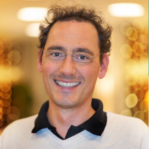 Lächelnder Mann mit Brille und lockigem Haar vor beleuchtetem Hintergrund