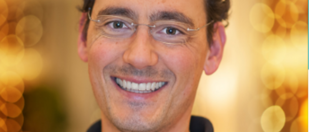 Lächelnder Mann mit Brille und lockigem Haar vor beleuchtetem Hintergrund