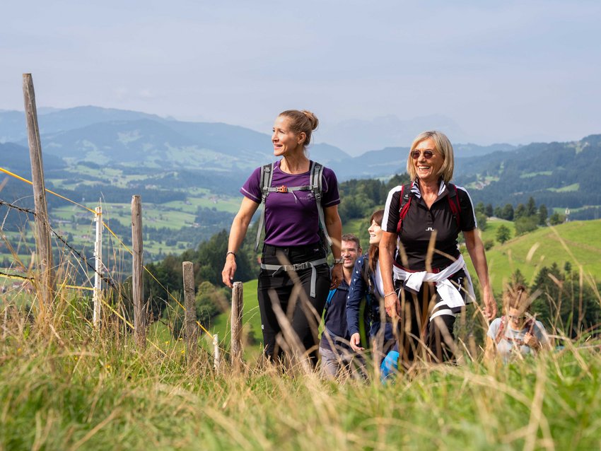 Gruppe von Menschen wandert auf einem Grasweg in einer bergigen Landschaft