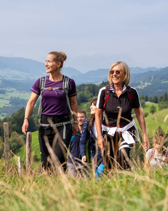 Gruppe von Menschen wandert auf einem Grasweg in einer bergigen Landschaft