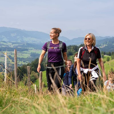 Group of people hiking on a grassy trail in a mountainous landscape