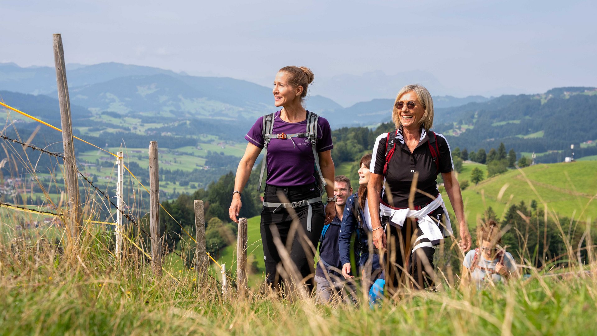 Group of people hiking on a grassy trail in a mountainous landscape