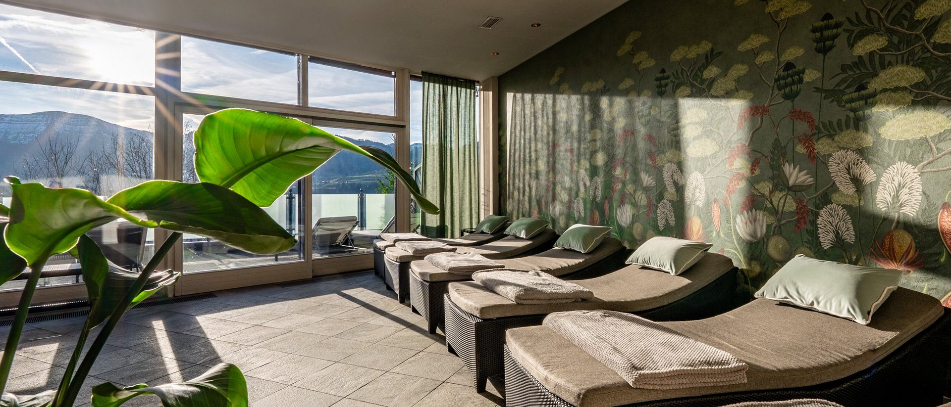 Your spa hotel in Allgäu: Allgäu Sonne Relaxation room with loungers, green plants, and mountain view in sunlight