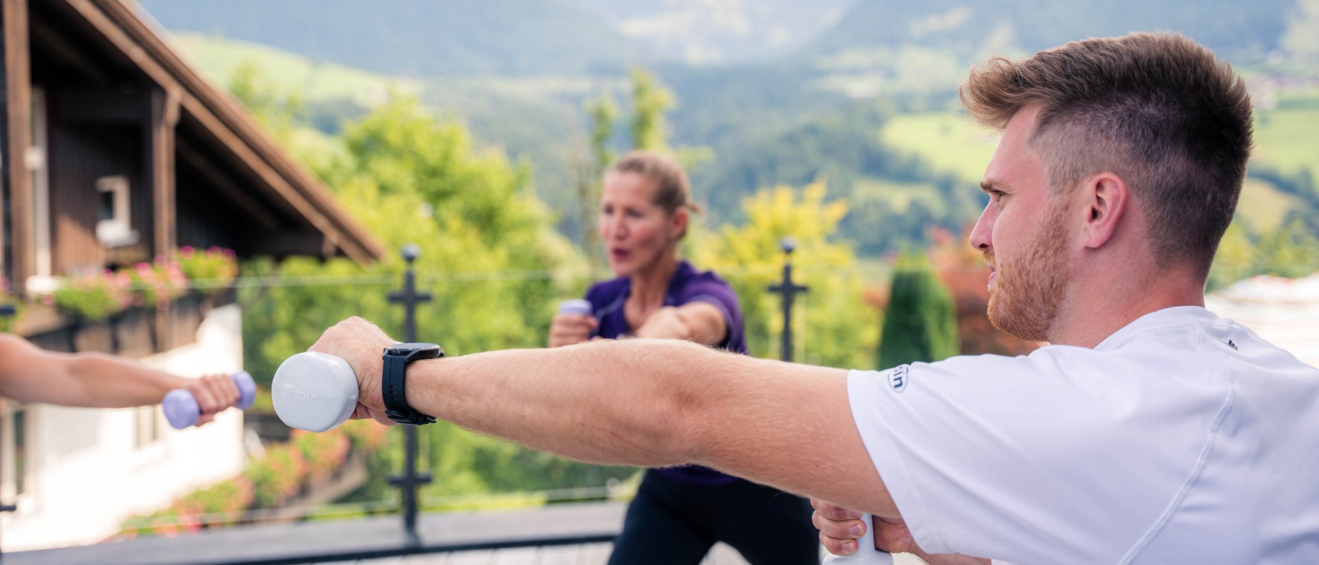 Gruppe trainiert mit Hanteln auf Terrasse vor Berglandschaft
