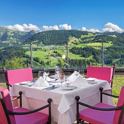 Esstisch mit rosa Stühlen auf Terrasse mit Bergblick bei sonnigem Wetter