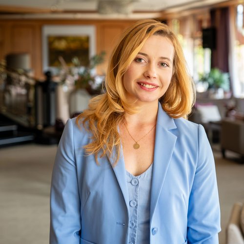 Unser Auftrag: Ihr perfekter Urlaub in Oberstaufen Lächelnde Frau in blauem Blazer in einem eleganten Hotel-Lobbybereich