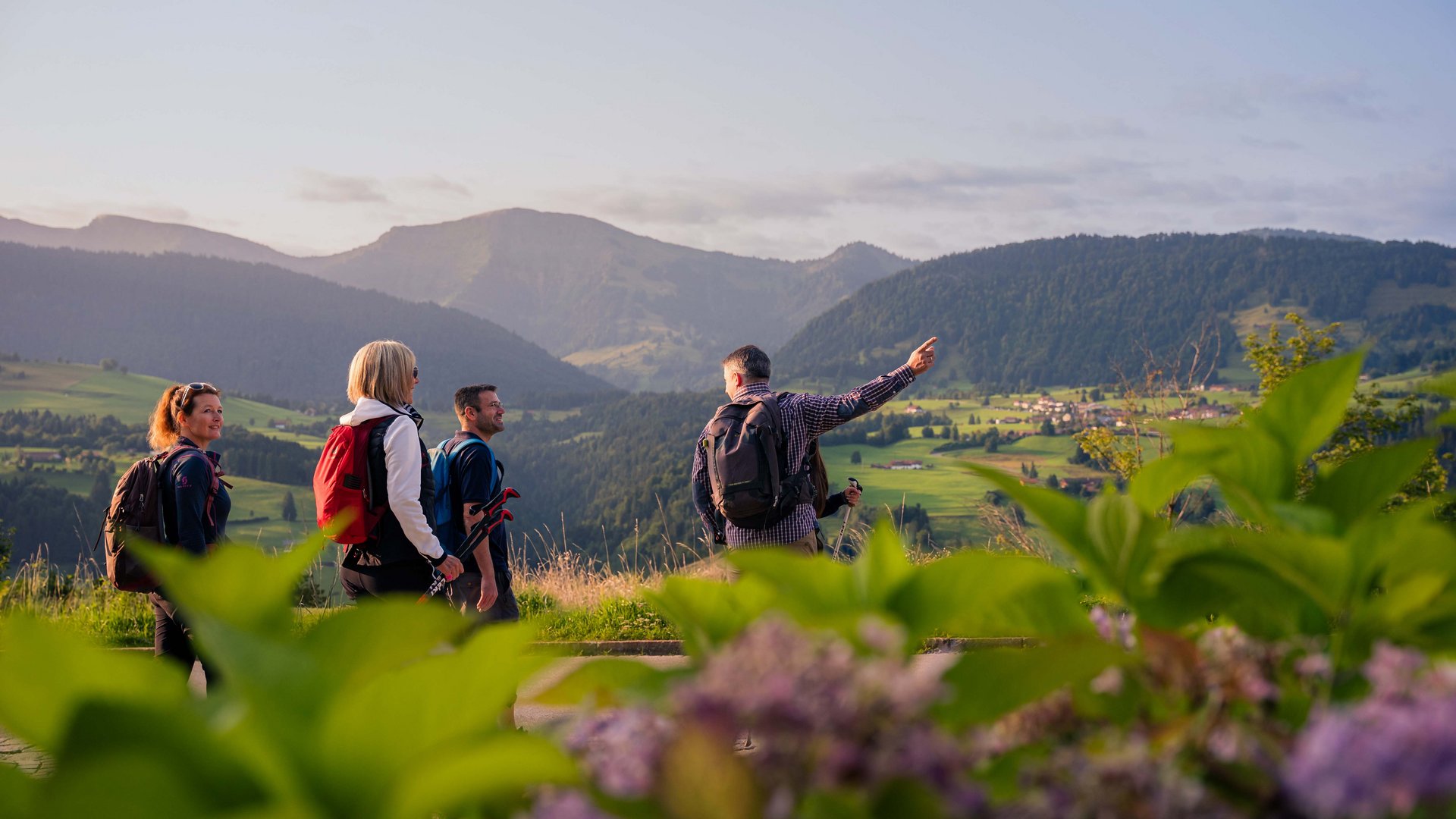 Four hikers with backpacks looking at green mountains and valley at sunset
