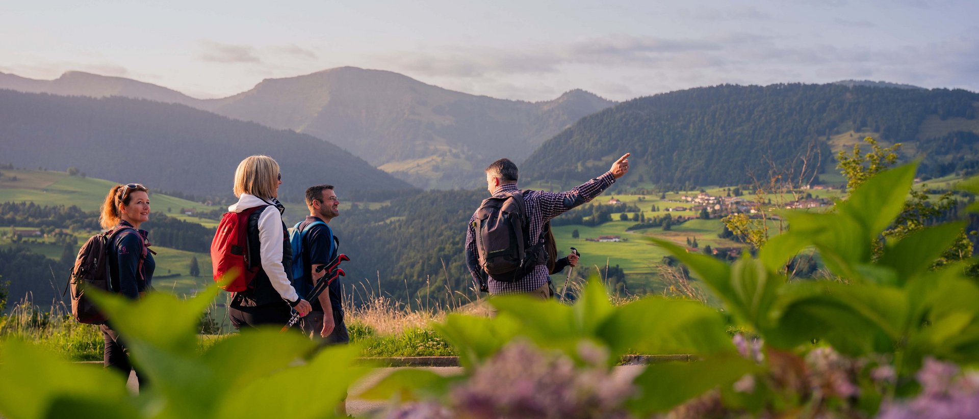 Vier Wanderer mit Rucksäcken blicken auf grüne Berge und Tal bei Sonnenuntergang