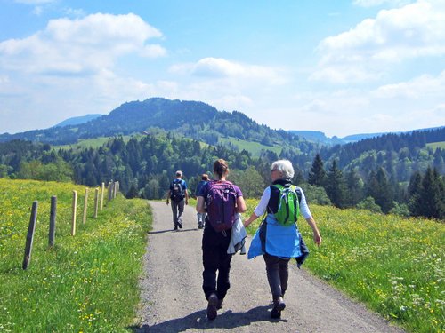 Menschen wandern auf einem Weg durch grüne Wiesen und Berge an einem sonnigen Tag