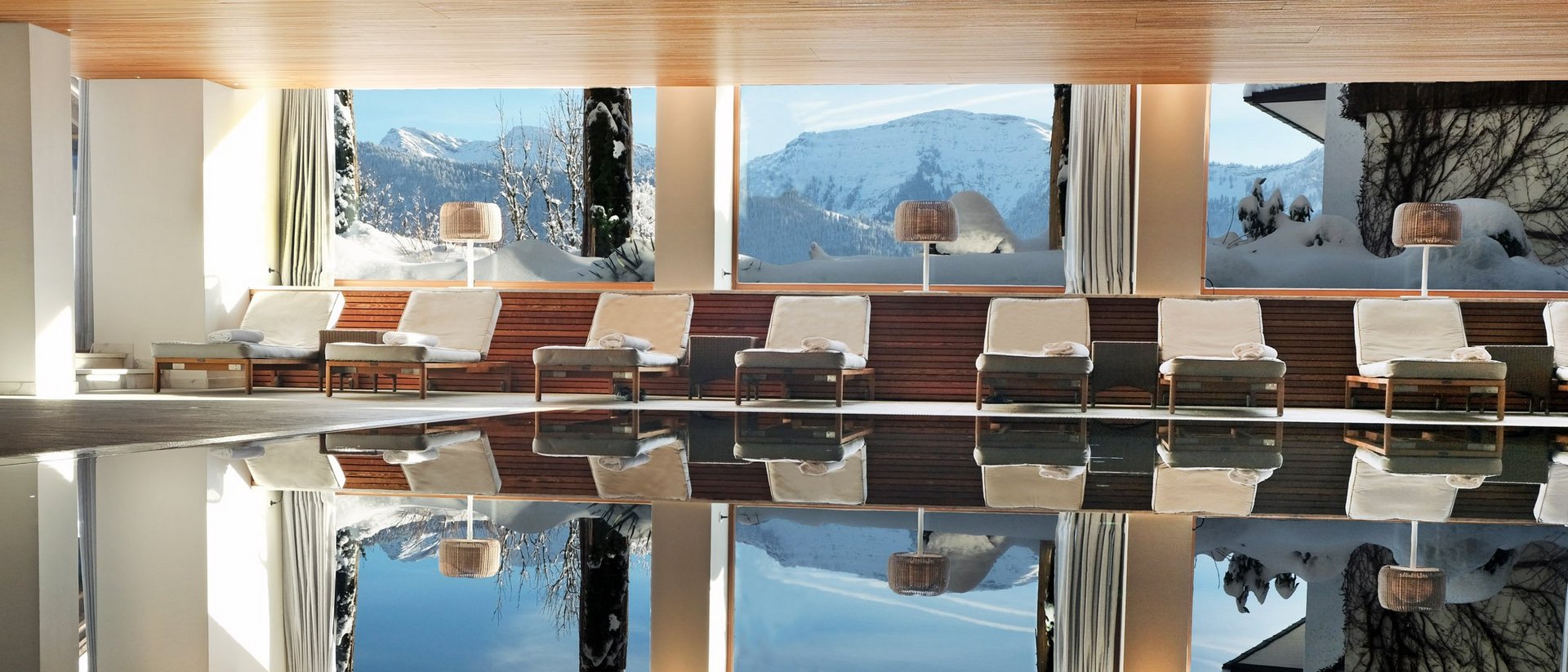 Innenpool mit Liegestühlen und Blick auf verschneite Berge durch große Fenster