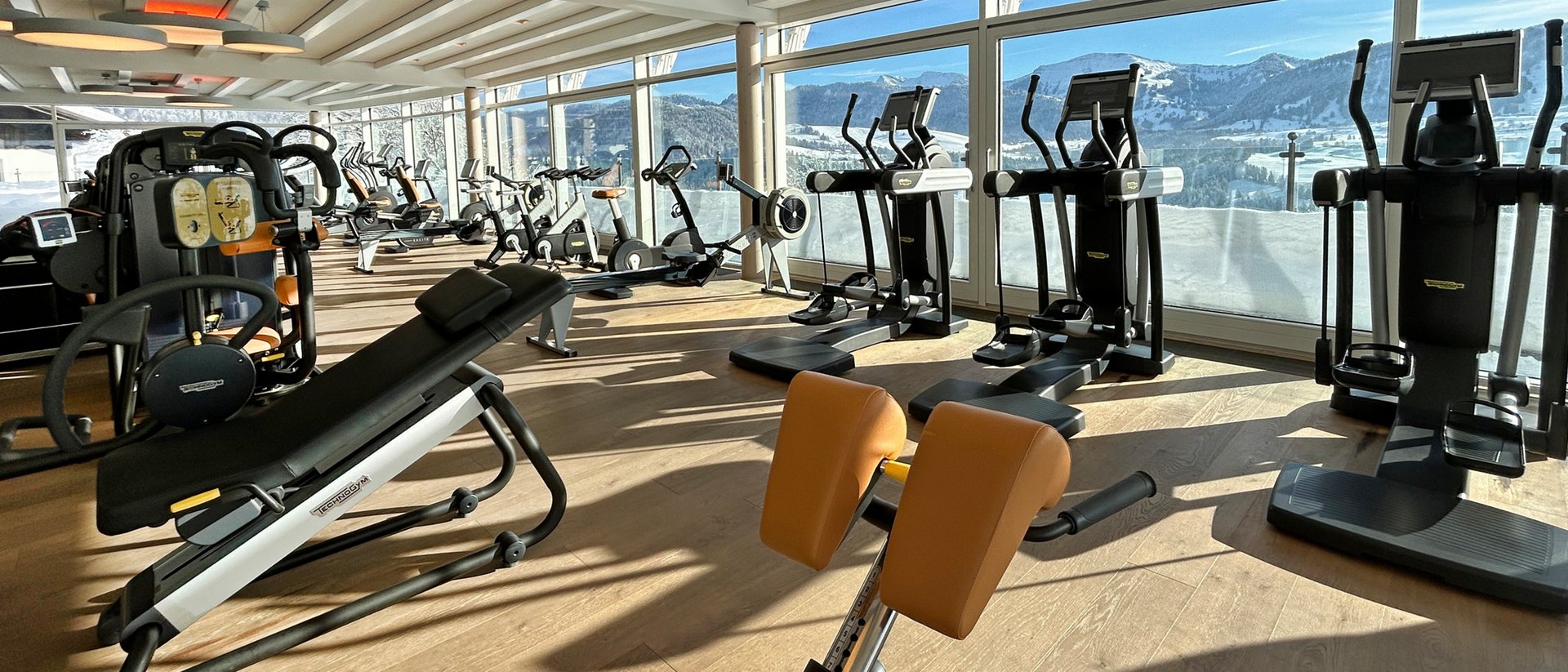 Helle Turnhalle mit Trainingsgeräten und Blick auf verschneite Berge