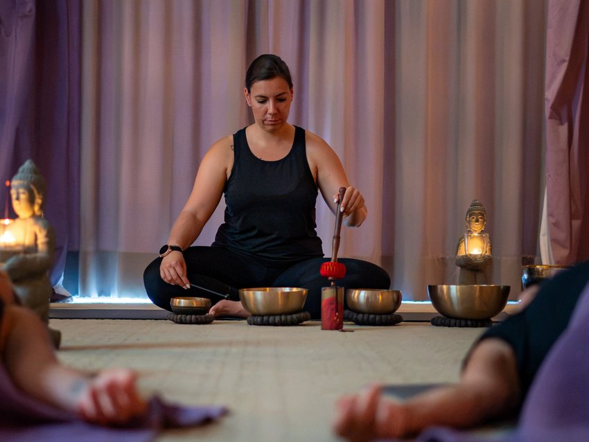 NEU: Yoga- & Ayurveda-Retreat Frau mit Klangschalen vor liegenden Teilnehmern und Buddhafiguren
