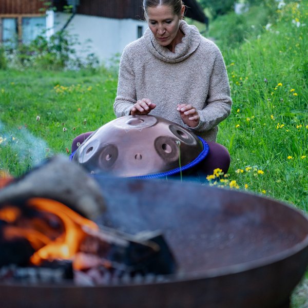 NEU: Yoga- & Ayurveda-Retreat Frau spielt im Garten ein Handpan-Instrument neben einer Feuerschale