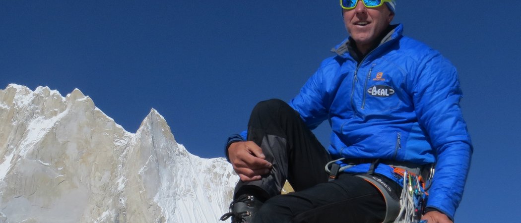 Bergsteiger in blauer Jacke auf Felsen mit schneebedecktem Berg und klarem Himmel