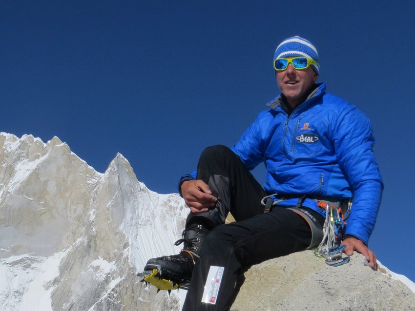 Bergsteiger in blauer Jacke auf Felsen mit schneebedecktem Berg und klarem Himmel