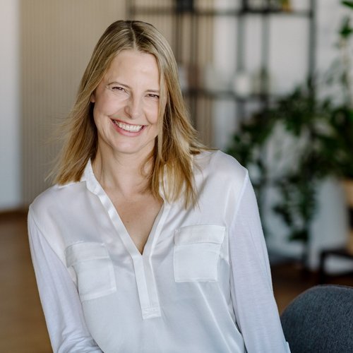 Lächelnde Frau mit weißer Bluse vor unscharfem Hintergrund im Innenraum