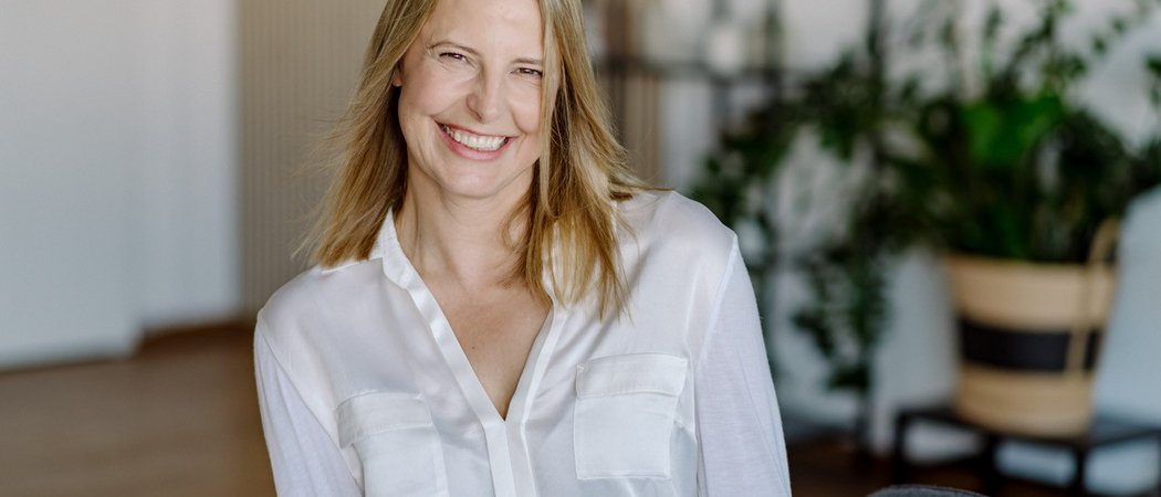 Lächelnde Frau mit weißer Bluse vor unscharfem Hintergrund im Innenraum
