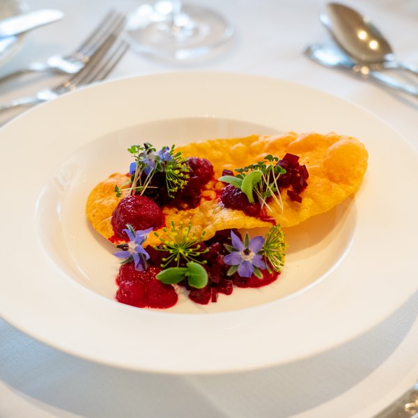 NEU: Yoga- & Ayurveda-Retreat Gourmetgericht mit knusprigem Teig, Beeren und essbaren Blüten auf einem weißen Teller