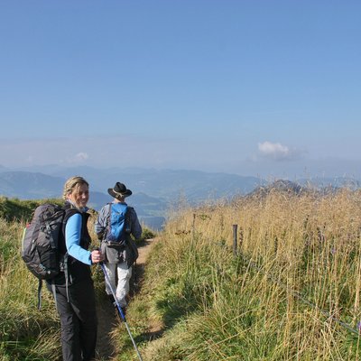 Zwei Wanderer auf Bergpfad mit Rucksack und Wanderstöcken bei klarem Himmel