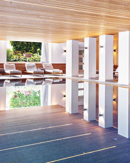Indoor pool area with lounge chairs and large windows showing outdoor greenery