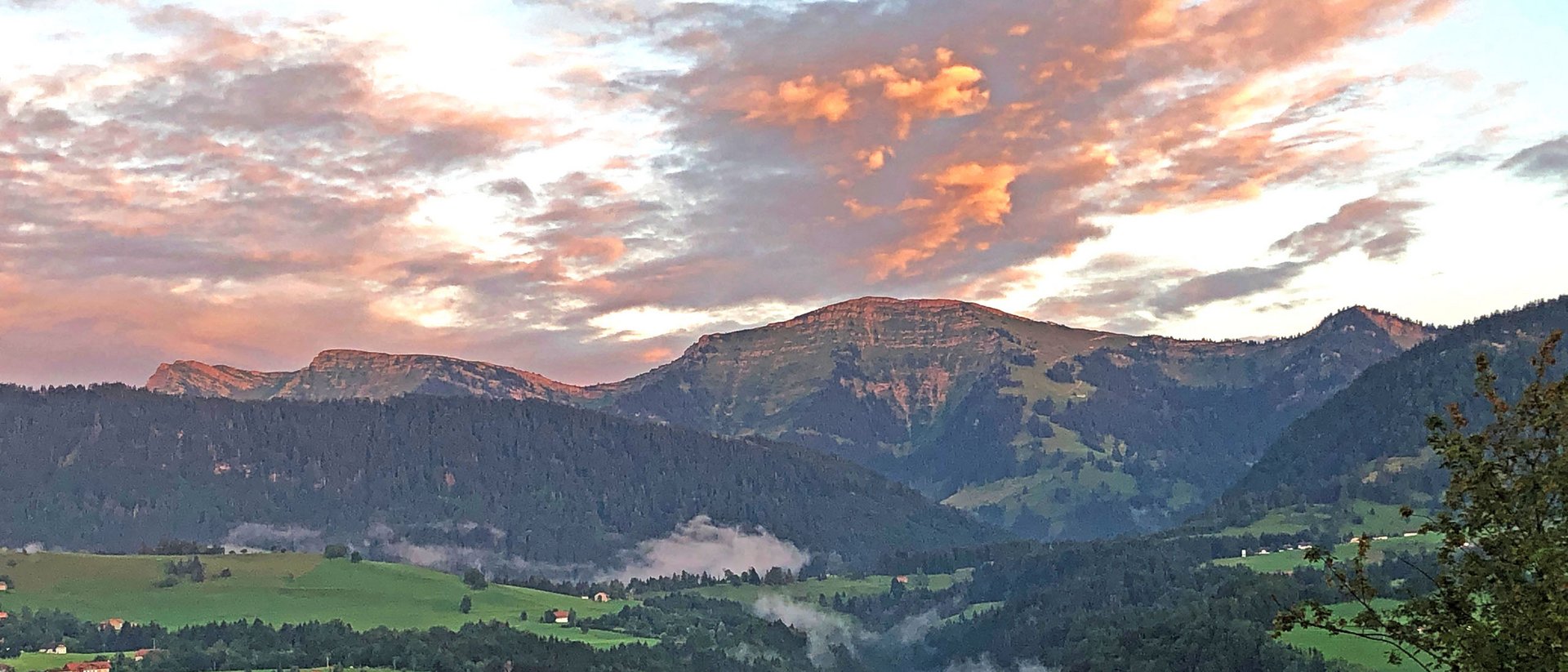 Berglandschaft mit grünen Wiesen und wolkigem Sonnenuntergangshimmel