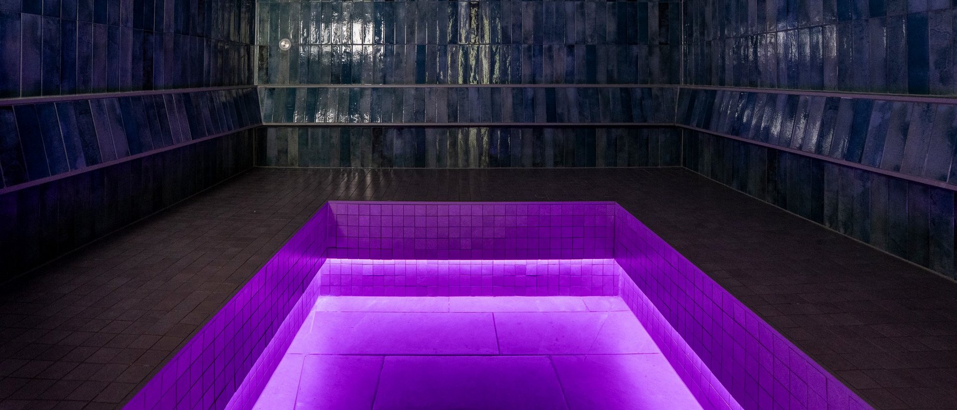 Your spa hotel in Allgäu: Allgäu Sonne Dark room with shiny blue tiles and a purple lit pool in the center