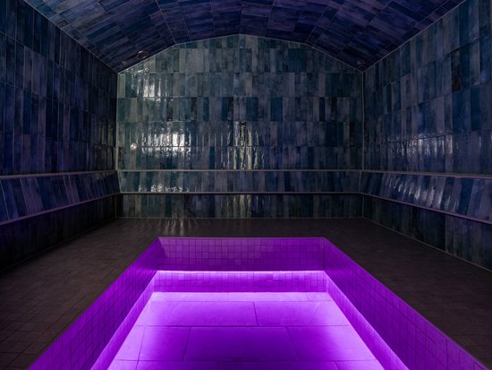 Your spa hotel in Allgäu: Allgäu Sonne Dark room with shiny blue tiles and a purple lit pool in the center