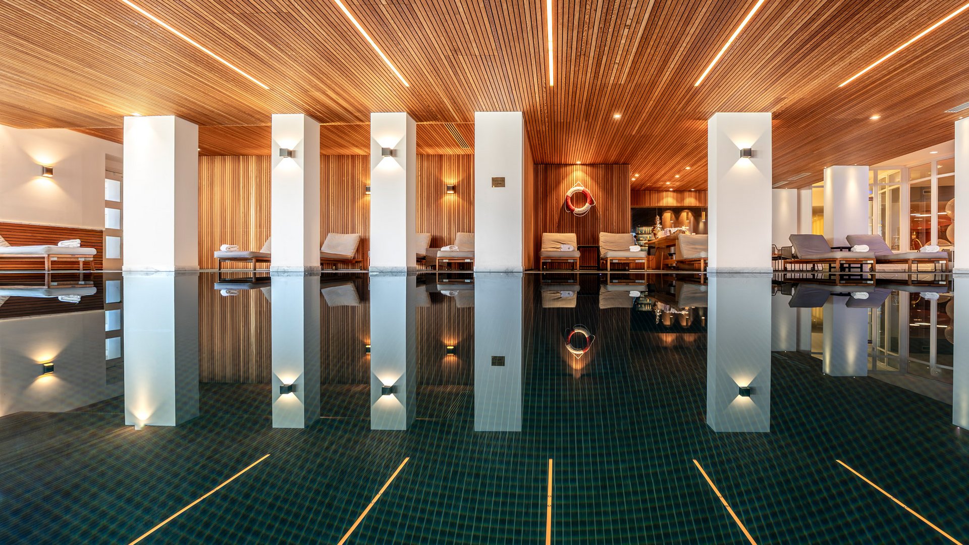 Moderner Innenpool mit Holzdecke und Liegestühlen neben weißen Säulen